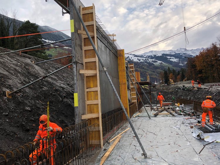 Foto: mehrere Arbeiter auf der Baustelle; hangseitig erstellte Beton-Wände der Notzufahrt 