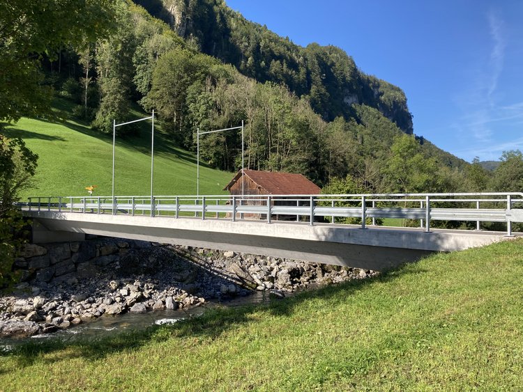 Photo: Completed concrete bridge; green meadows and forests in the background and the river Muota below the bridge.