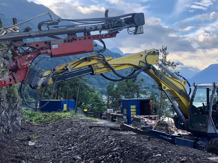 Foto: Ankerbohrgerät im Einsatz in steilem Gelände; im Hintergrund Urnersee, Gebirge, bewölkter Himmel