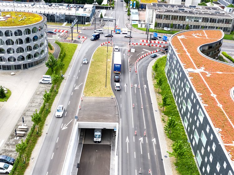 Photo: Aerial view of the tunnel entrance and the road junction above; in the background a settlement. 